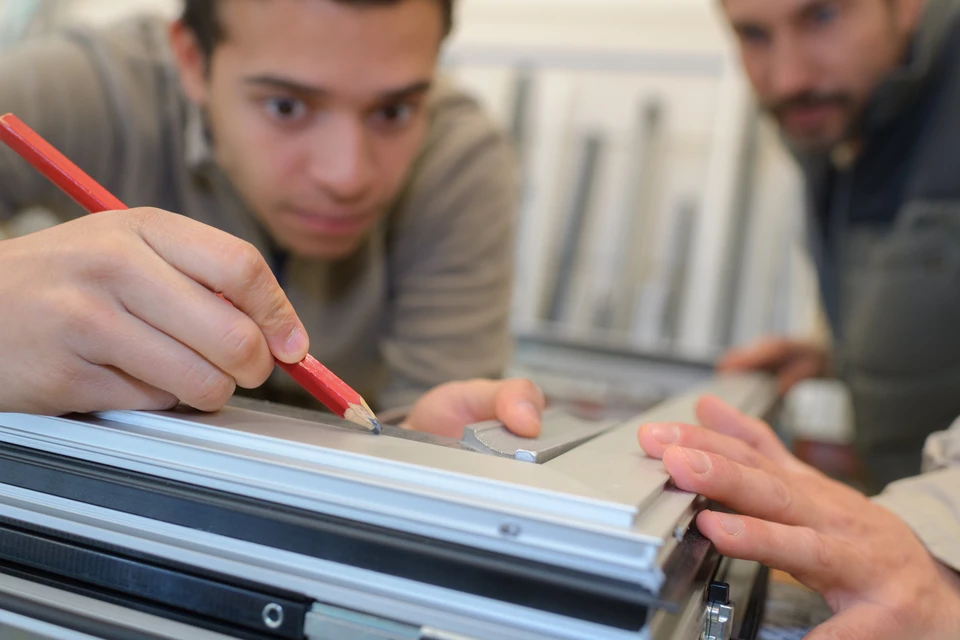 Scène d'atelier avec artisan utilisant crayon rouge pour tracer sur surface métallique