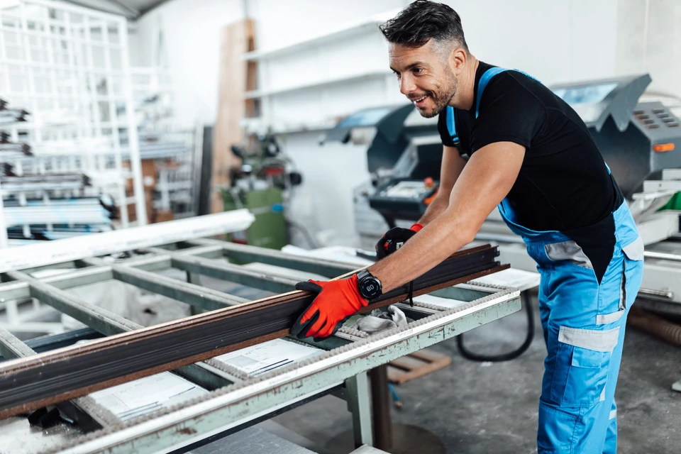 Le travailleur manuel travaille dans une usine de menuiserie, il monte des fenêtres et des portes en PVC